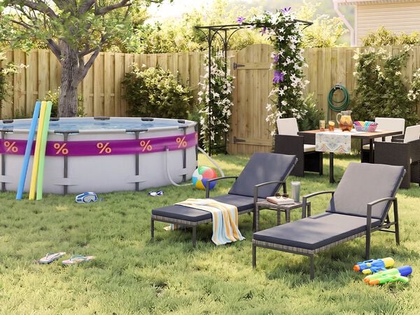 Zonnige achtertuin met opzetzwembad, zwembadnoodles, zwembril, strandbal en slippers in het gras. Twee zwarte metalen ligstoelen met grijze kussens staan naast een klein bijzettafeltje, terwijl een tuinset met donkere gevlochten stoelen is geplaatst bij een bloeiende pergola, houten schutting en groene tuinplanten.