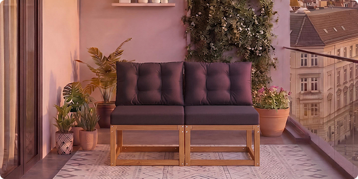 Tweepersoonsmodulaire houten bank met donkergrijze kussens op een balkon omringd door potplanten en stadsgezicht op de achtergrond