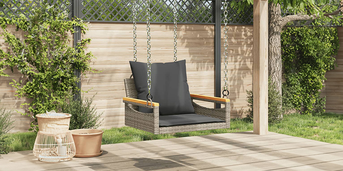 Schommelbank in rattan voor buiten met donkere kussens op een terras. Klik om de collectie te bekijken.